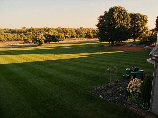 A wide lawn mowed in crisp stripes with a ride-on mower parked at the edge